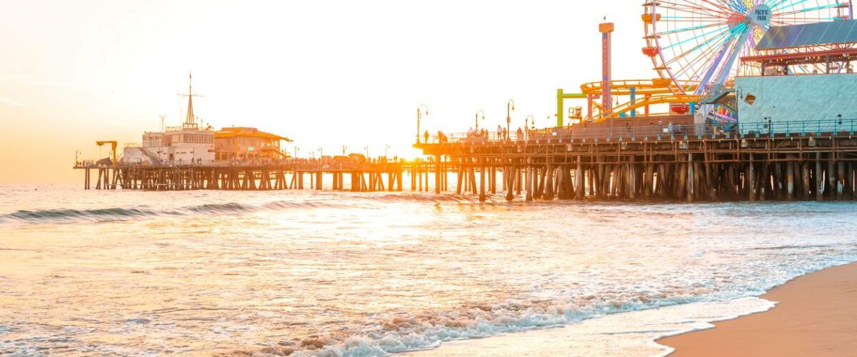 A beachfront view of Santa Monica Pier in Los Angeles, CA, at sunset.