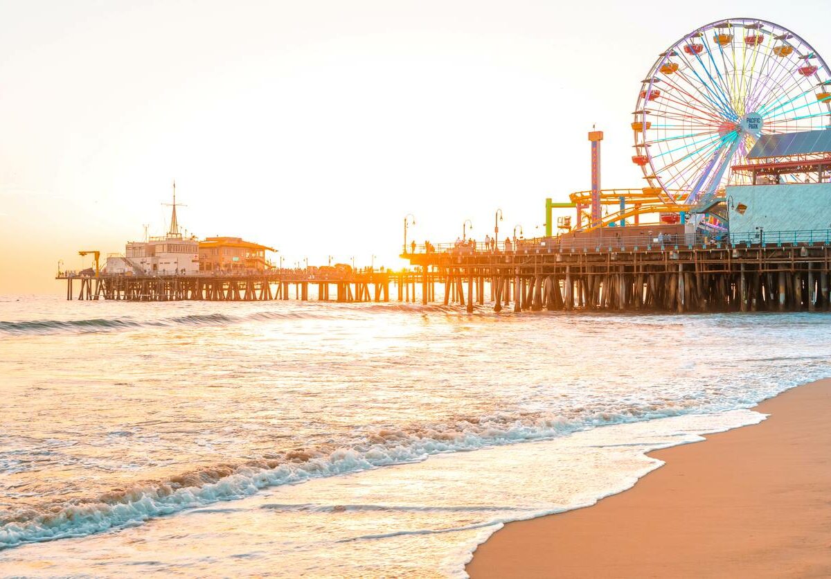 A beachfront view of Santa Monica Pier in Los Angeles, CA, at sunset.