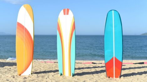 Three colorful surfboards standing upright in the sand on a sunny beach.