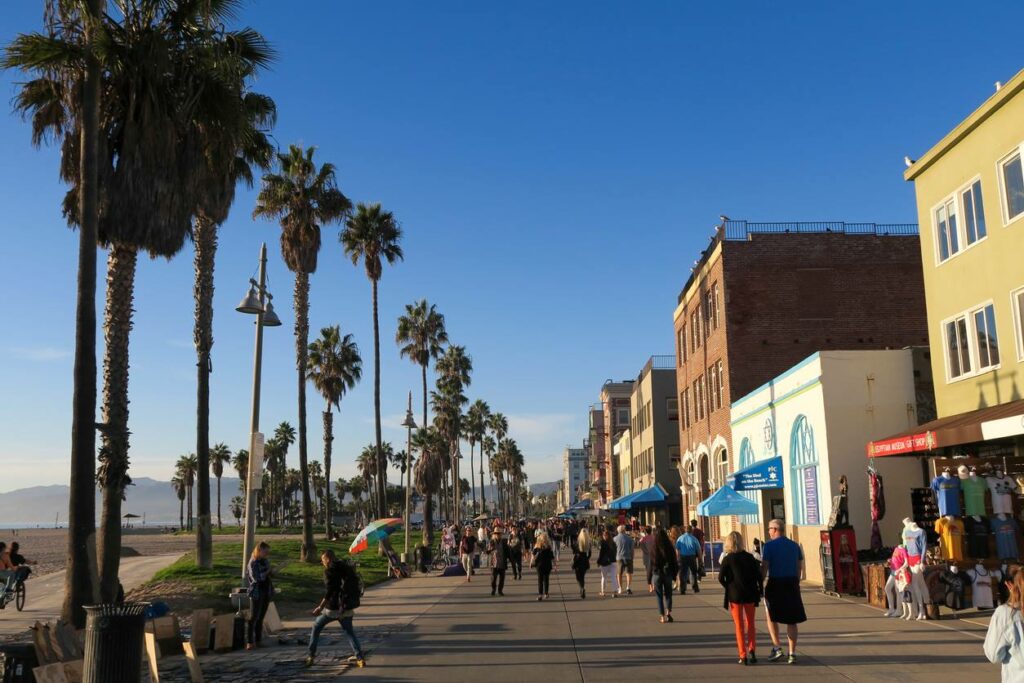 A busy pedestrian street lined with palm trees along Venice Beach.