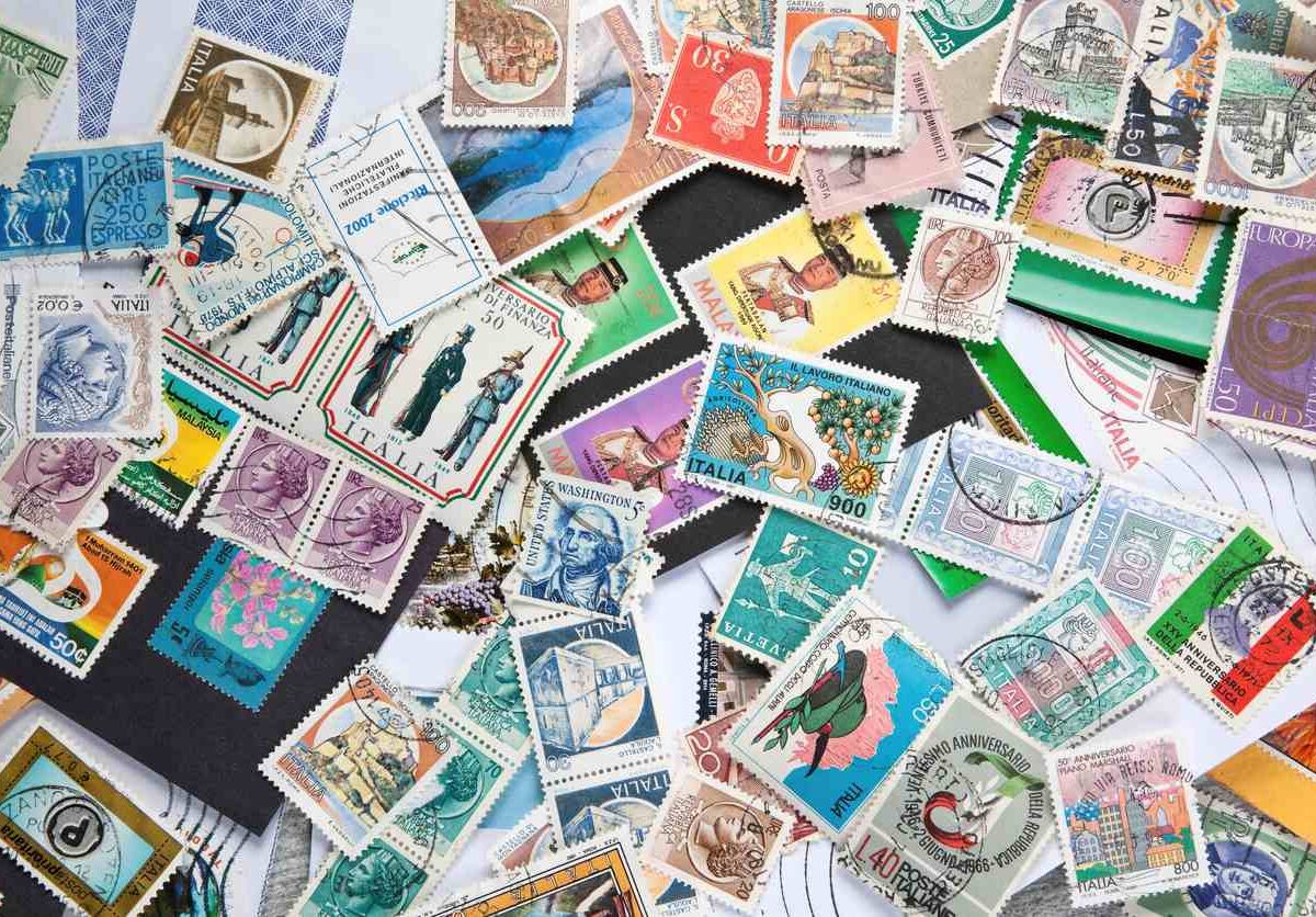 Old and new postage stamps from different countries are scattered about a table.