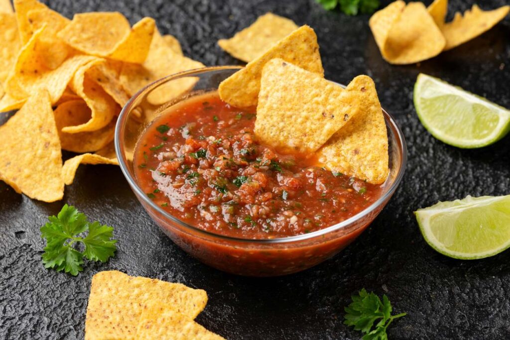 An arrangement of tortilla chips and tomato salsa with lime and cilantro on a table.