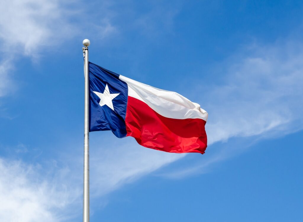 The Texas state flag is raised high, waving against a blue sky.