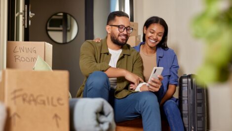 Smiling couple looking at smartphone while relaxing during a move.