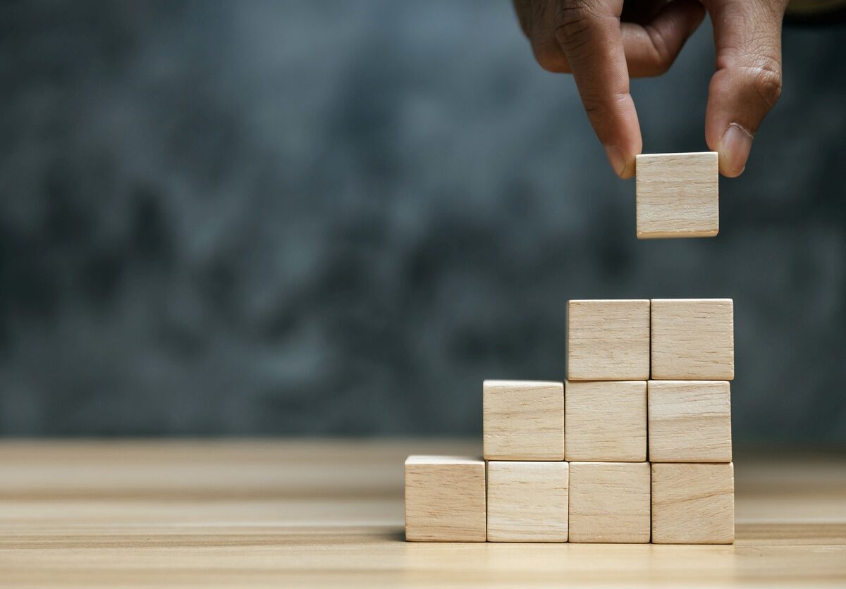 A hand stacks wooden blocks in a row of columns.
