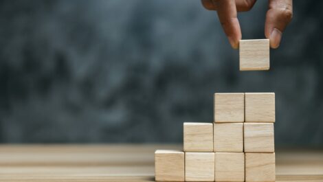 A hand stacks wooden blocks in a row of columns.